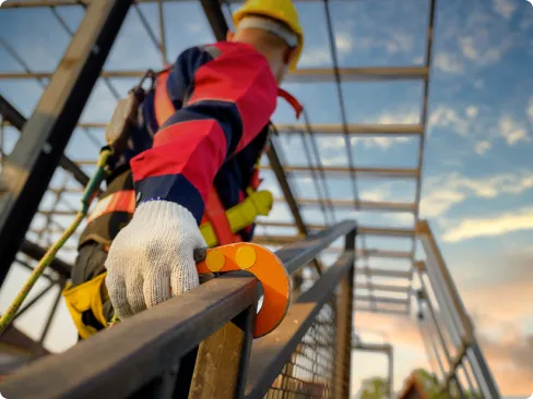 Homem em obra subindo as escadas com o equipamento de segurança preso ao corrimão.
