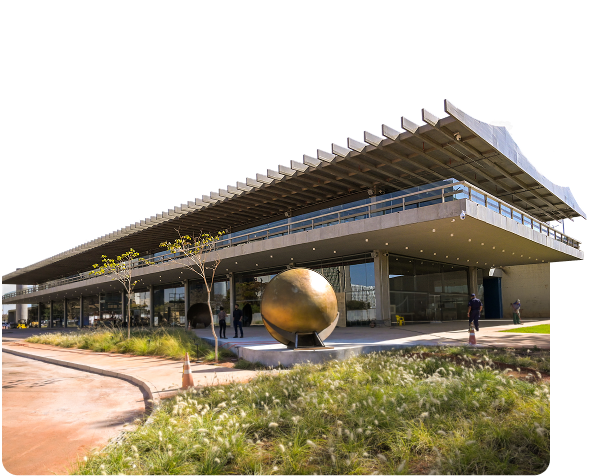 A fachada do SESI Lab, um prédio de arquitetura moderna com um teto de concreto e grandes janelas de vidro. Em frente, há uma escultura esférica dourada em uma área com grama.